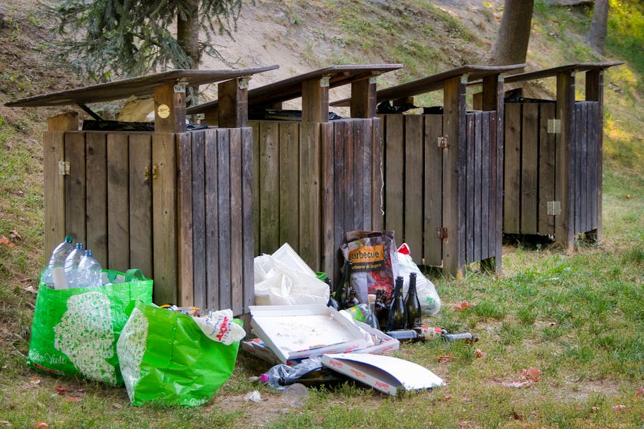 A large pile of black plastic rubbish bags stacked against a modern exterior wall composed of smooth, beige tiles with visible grout lines. The bags are tightly sealed and some appear slightly bulging